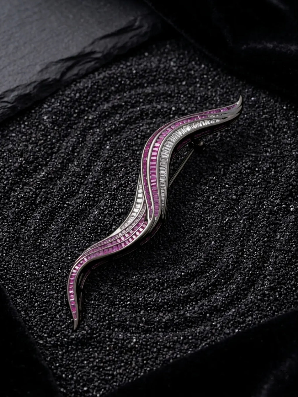 A curved silver-toned brooch or hair pin with rows of pink gemstones and clear stones, displayed on a textured black surface.